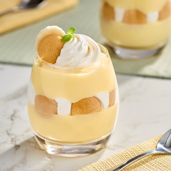 A glass of banana pudding dessert layered with vanilla wafers and whipped cream, garnished with a wafer and mint.