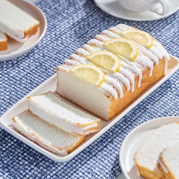 A loaf of lemon pound cake topped with icing, powdered sugar, and lemon slices, served on a rectangular plate.