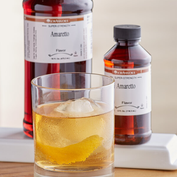 A glass of liquid with ice and a lemon wedge next to a bottle of LorAnn Oils Amaretto Flavor.