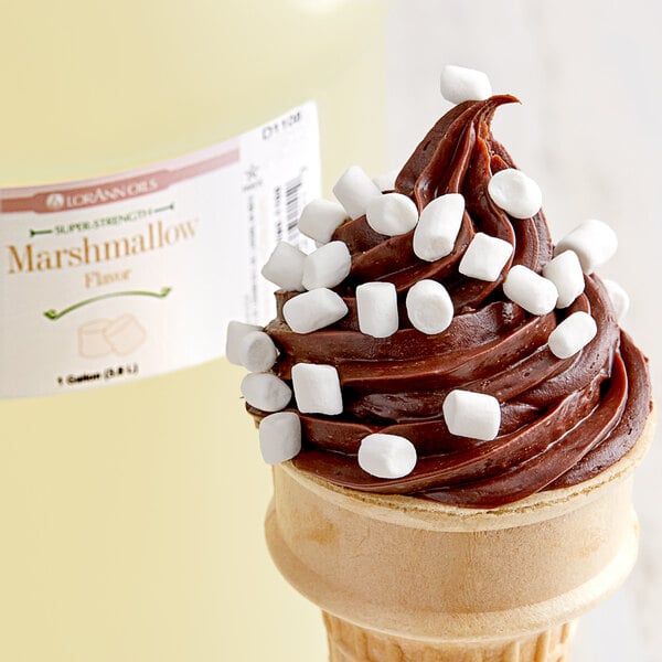 A chocolate ice cream cone with marshmallows on top drizzled with chocolate syrup.