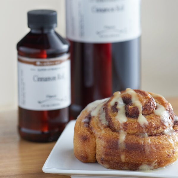 A cinnamon roll on a plate next to a bottle of LorAnn Oils Cinnamon Roll flavor.