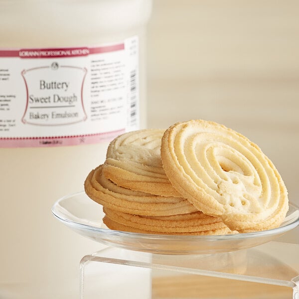 A plate of butter cookies with swirls on a glass plate with a jar of LorAnn Buttery Sweet Dough Emulsion.