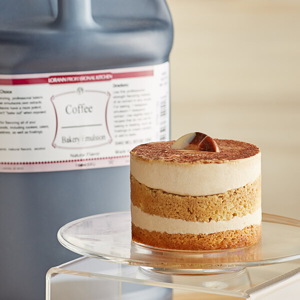 A cake on a glass plate next to a large bottle of LorAnn Oils All-Natural Coffee Bakery Emulsion.