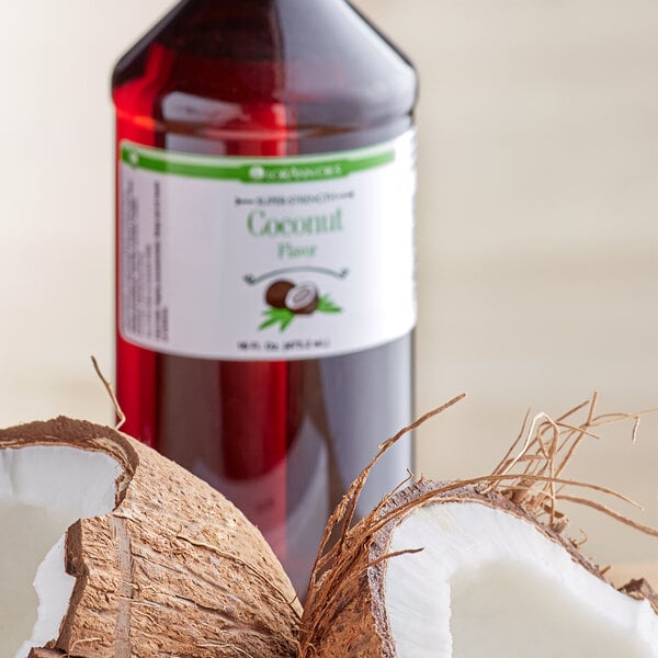 A close up of a bottle of LorAnn Oils Coconut Super Strength Flavor next to a coconut with a broken shell.