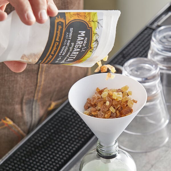 A person pouring a mixture of brown and white crystals into a glass funnel.