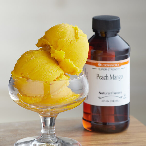 A glass of yellow peach mango ice cream next to a bottle of LorAnn Peach Mango flavor.