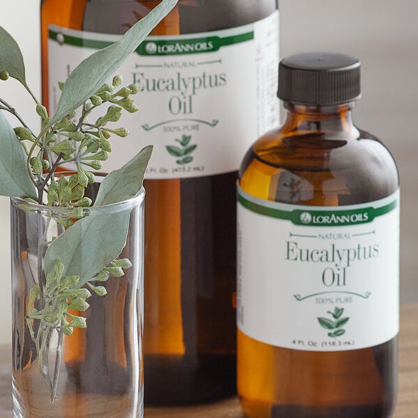 A close-up of a LorAnn Oils Eucalyptus flavor bottle next to a glass of water with eucalyptus leaves.