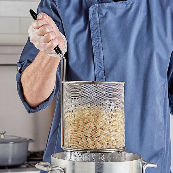 A person in a blue uniform using a Choice stainless steel strainer / blanching basket to cook food.