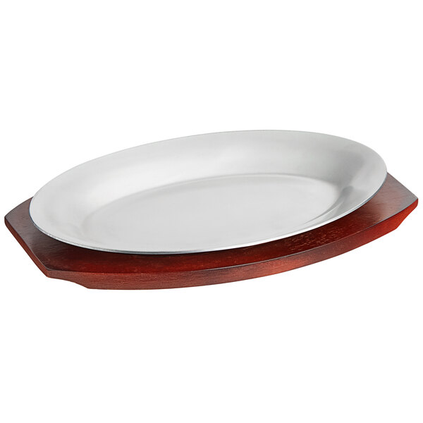 A white oval aluminum sizzler platter on a mahogany finish rubberwood surface.