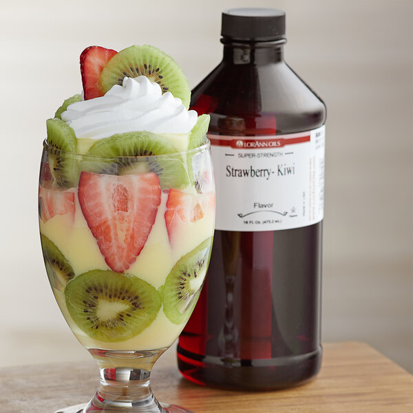 A glass of fruit with red liquid next to a bottle of LorAnn Oils Strawberry Kiwi flavor.