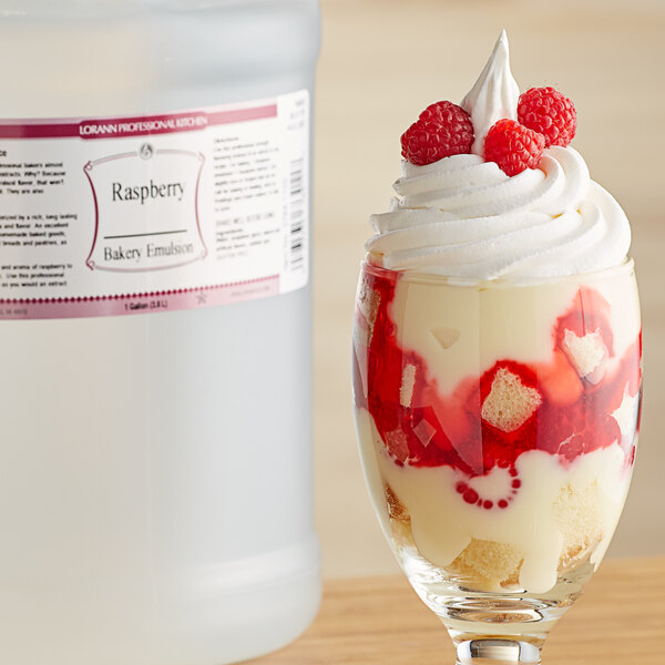 A glass of raspberry trifle next to a bottle of LorAnn Oils Raspberry Bakery Emulsion.