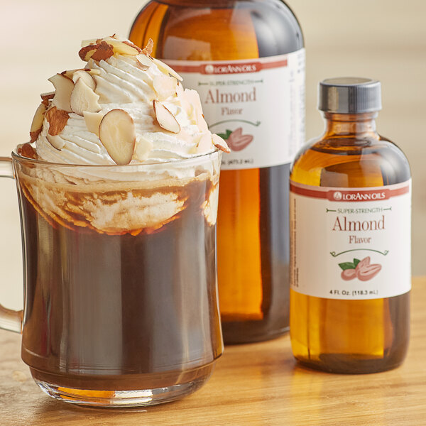 A glass mug of coffee with whipped cream and a bottle of LorAnn Bitter Almond Flavor on a table.