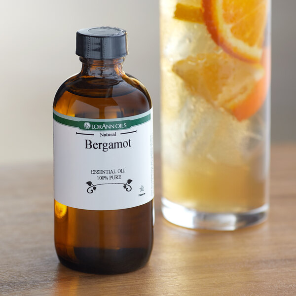 A bottle of LorAnn Oils All-Natural Bergamot Super Strength Flavor next to a glass of liquid with orange slices.