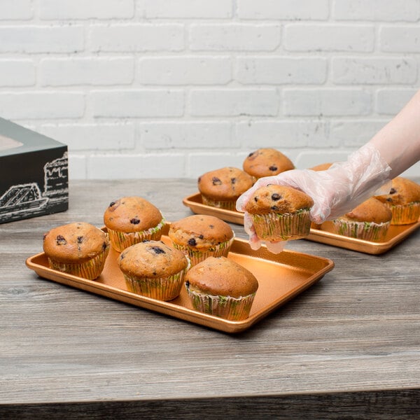 A person holding a Chicago Metallic bakery display tray with muffins.