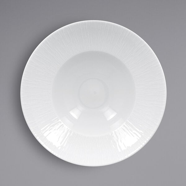 A close-up of a white RAK Porcelain Soul extra deep plate with an embossed pattern on the rim.