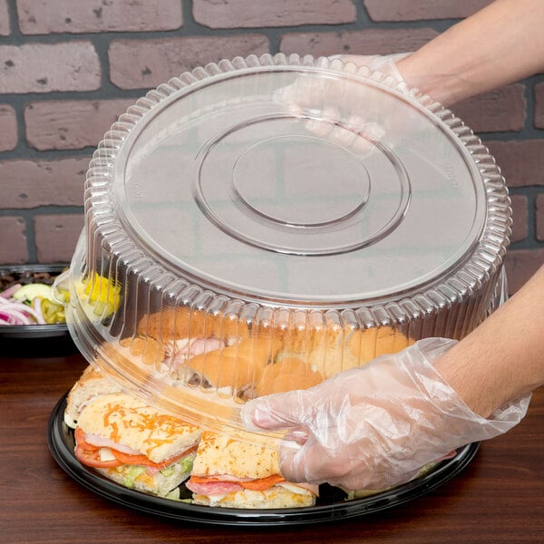 A hand in a plastic glove putting a sandwich into a Sabert clear plastic container.