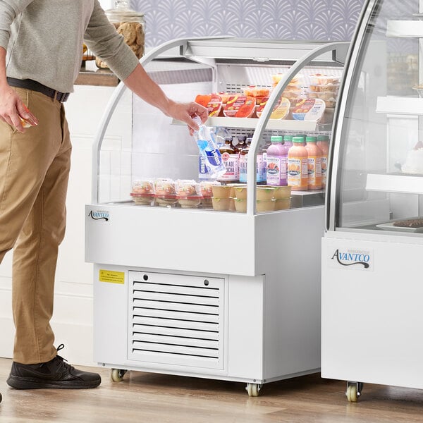 A man standing next to an Avantco white horizontal air curtain merchandiser filled with food.