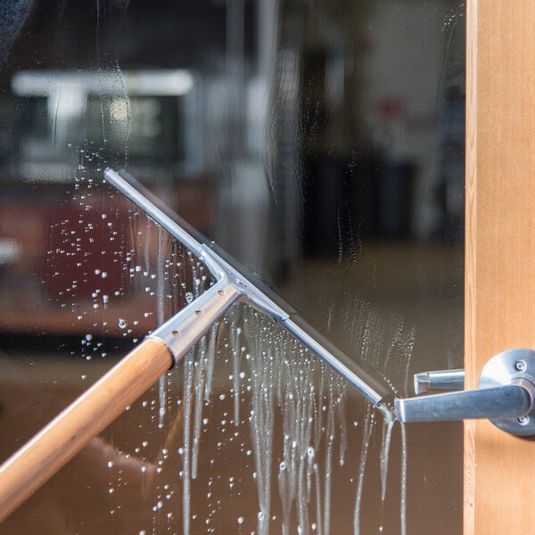 A 12-inch window squeegee with a steel handle being used to clean a glass door.