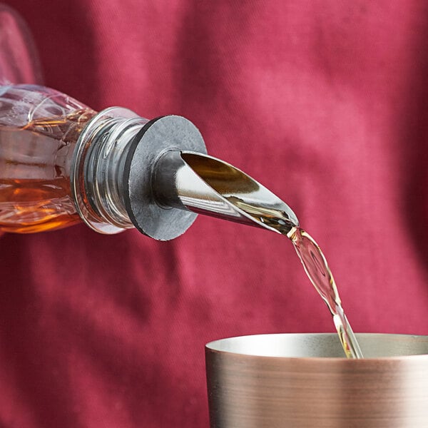 A person using an American Metalcraft stainless steel liquor pourer to pour liquid into a cup.