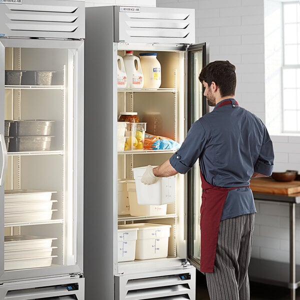 A man opening the glass door of a Beverage-Air reach-in refrigerator in a professional kitchen.