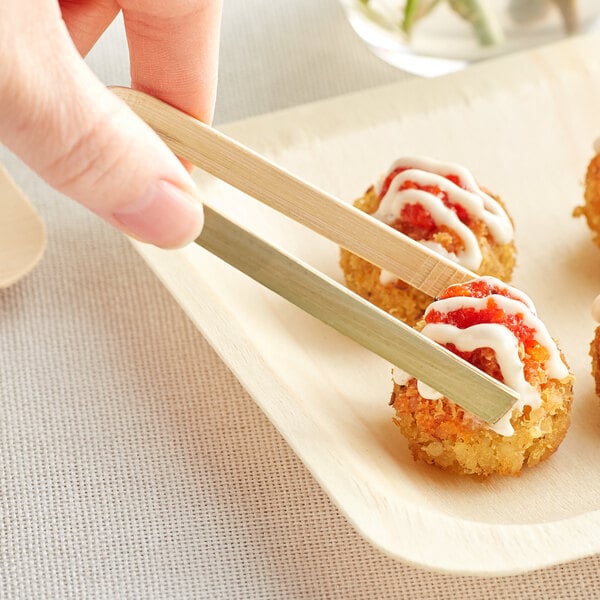 Bamboo tongs holding food on a plate.