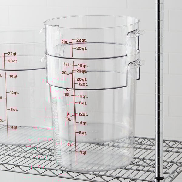 Three Cambro clear round food storage containers on a metal shelf.