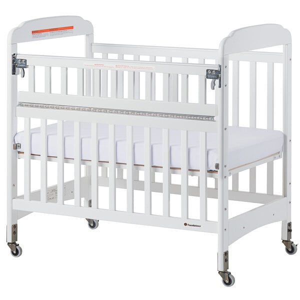 A white Foundations Serenity SafeReach wood crib with a white sheet on the mattress.