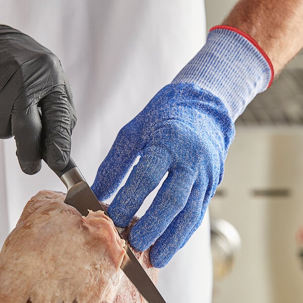 A person wearing Mercer Culinary blue cut-resistant gloves cutting meat with a knife.