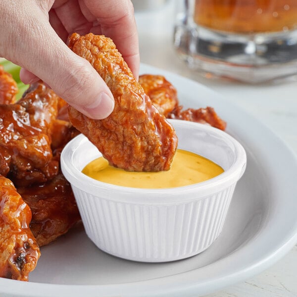 A hand dipping a piece of chicken into a white cup with sauce.