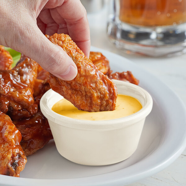 A hand dipping a piece of chicken into a white Acopa melamine ramekin of sauce.