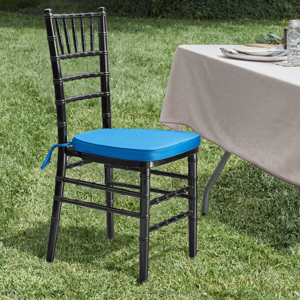 A Lancaster Table & Seating Black Wood Chiavari Chair with a blue cushion on a table with a white tablecloth in the grass.