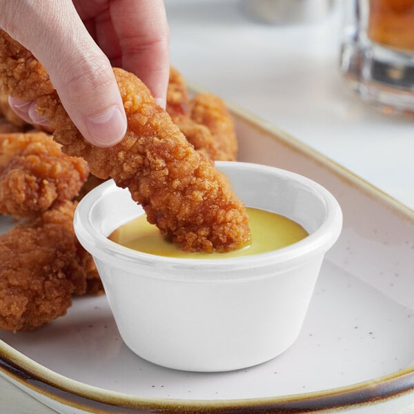 A person dipping a chicken finger into a white bowl of sauce.