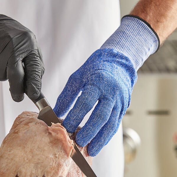 A person wearing Mercer Culinary Millennia Fit blue cut-resistant gloves cutting meat on a counter.
