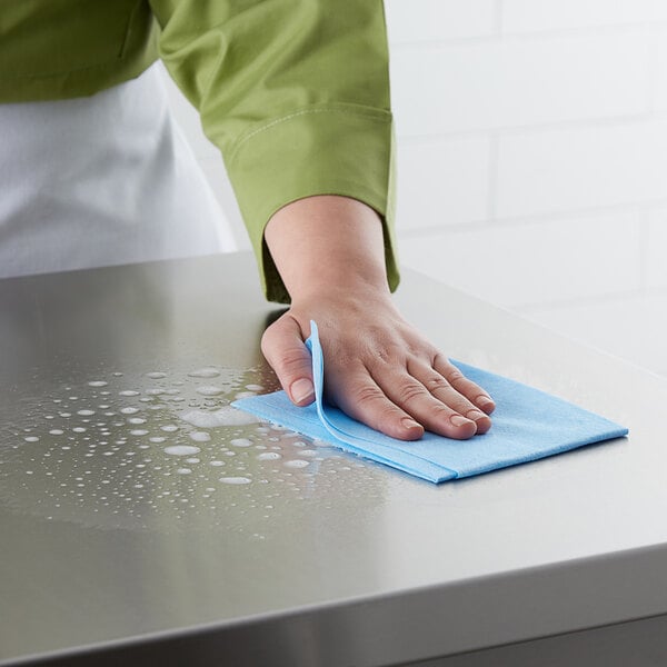 A hand wiping a counter in a professional kitchen with a blue ChoiceHD wiper.