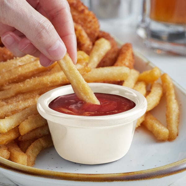 A person dipping a french fry into a white Acopa ramekin filled with ketchup.