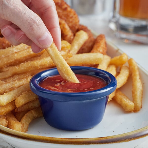 a person dipping a french fries into a blue bowl with ketchup