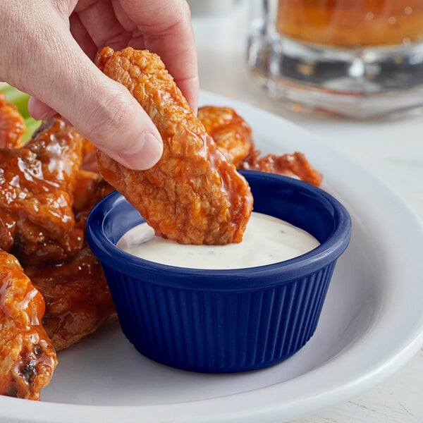 A person dipping a piece of chicken into a blue Acopa fluted ramekin of sauce.