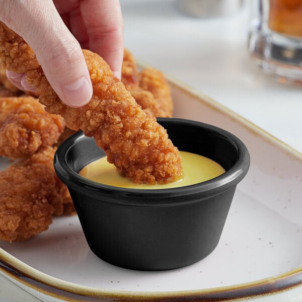 A person dipping a chicken finger into a black Acopa ramekin of sauce.