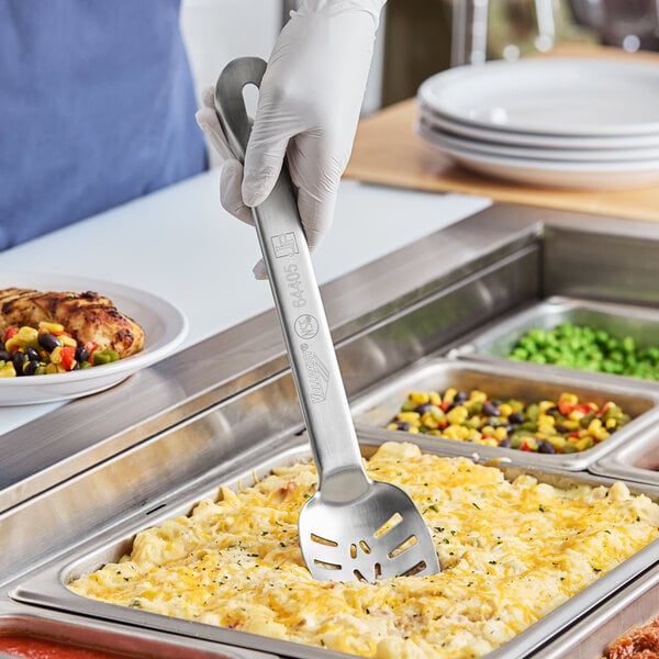 A person in gloves holding a Vollrath Jacob's Pride slotted stainless spoon over food on a plate.