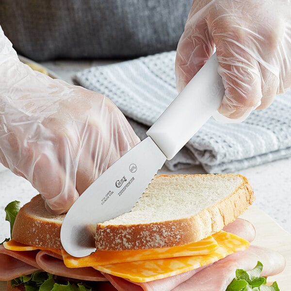 A person cutting a sandwich with a Choice scalloped sandwich spreader.