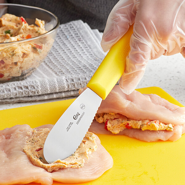 A Choice stainless steel sandwich spreader with a yellow handle being used to spread food on a yellow cutting board.