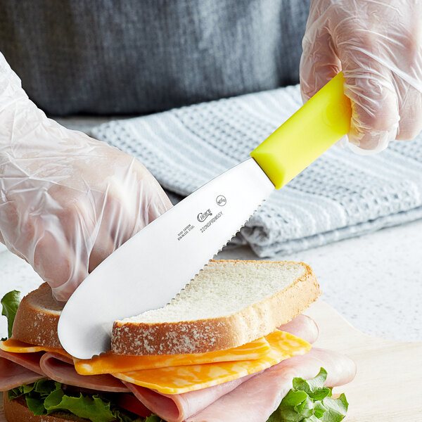 A person slicing a sandwich with a Choice Scalloped Sandwich Spreader.