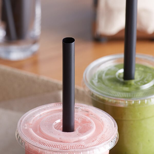 Two plastic cups with Choice black straws on a table with drinks.