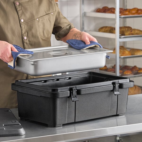 A black top-loading insulated food pan carrier with a stainless steel food pan and lid being placed inside.