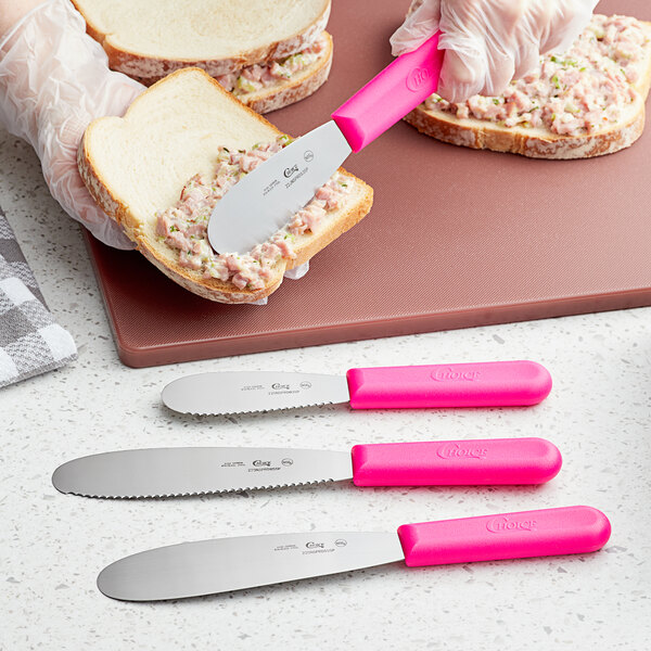 A person using a Choice sandwich spreader with a neon pink handle to spread food on a piece of bread.