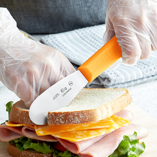 A person using a Choice Scalloped Sandwich Spreader to cut a sandwich.