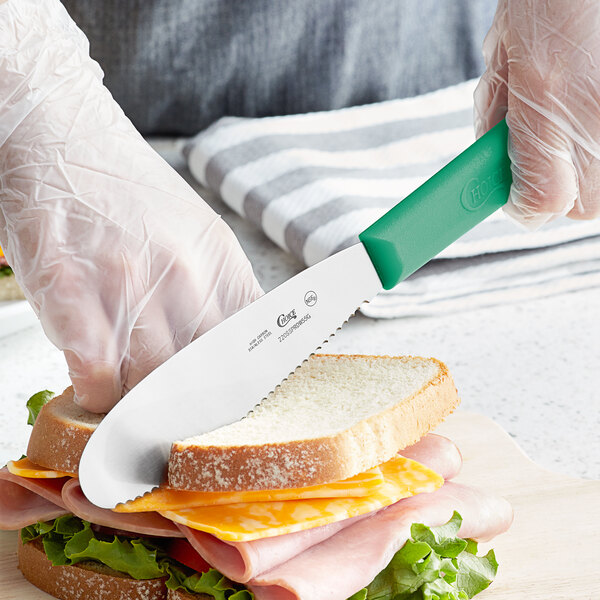 A person using a Choice scalloped sandwich spreader to cut a sandwich.