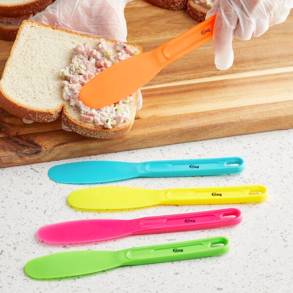A person using a Choice blue sandwich spreader to spread on a sandwich.