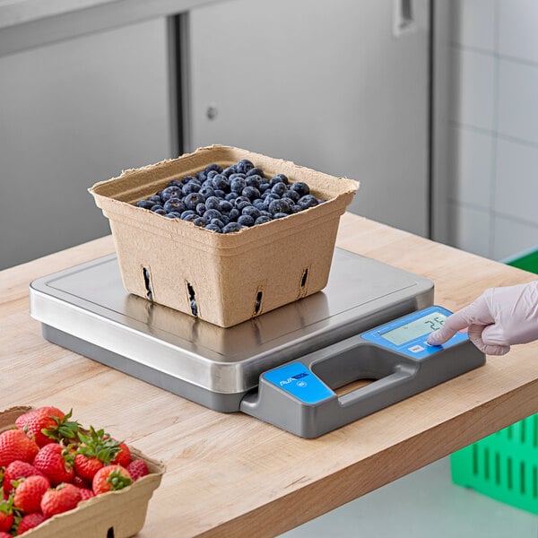 A person using an AvaWeigh digital portion scale to weigh strawberries on a counter.