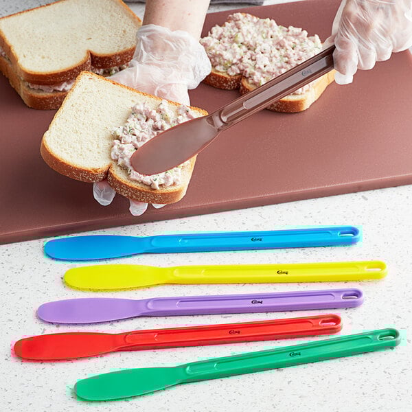 A person spreading spread on a sandwich with a Choice brown polypropylene sandwich spreader.